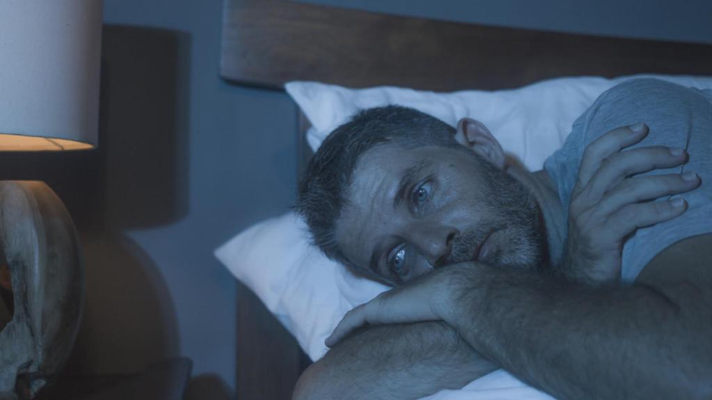 Imagen de un hombre en la cama mirando al vacío por culpa del insomnio. iStock