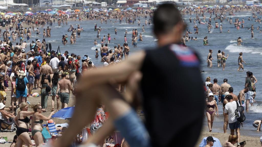 Una persona observa una playa valenciana llena de gente.