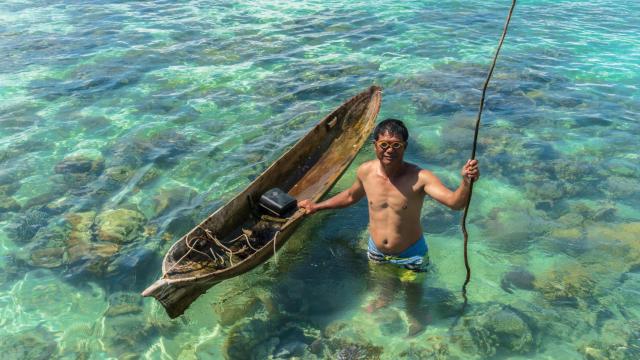 Un pescador de Bajau Laut posa con su barco de madera en las aguas turquesas de Semporna.