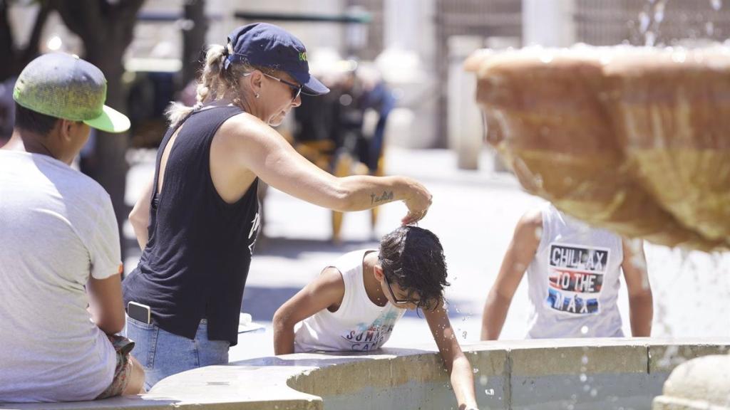 Una madre y su hijo se refrescan en una fuente con agua en una jornada marcada por las altas temperaturas.
