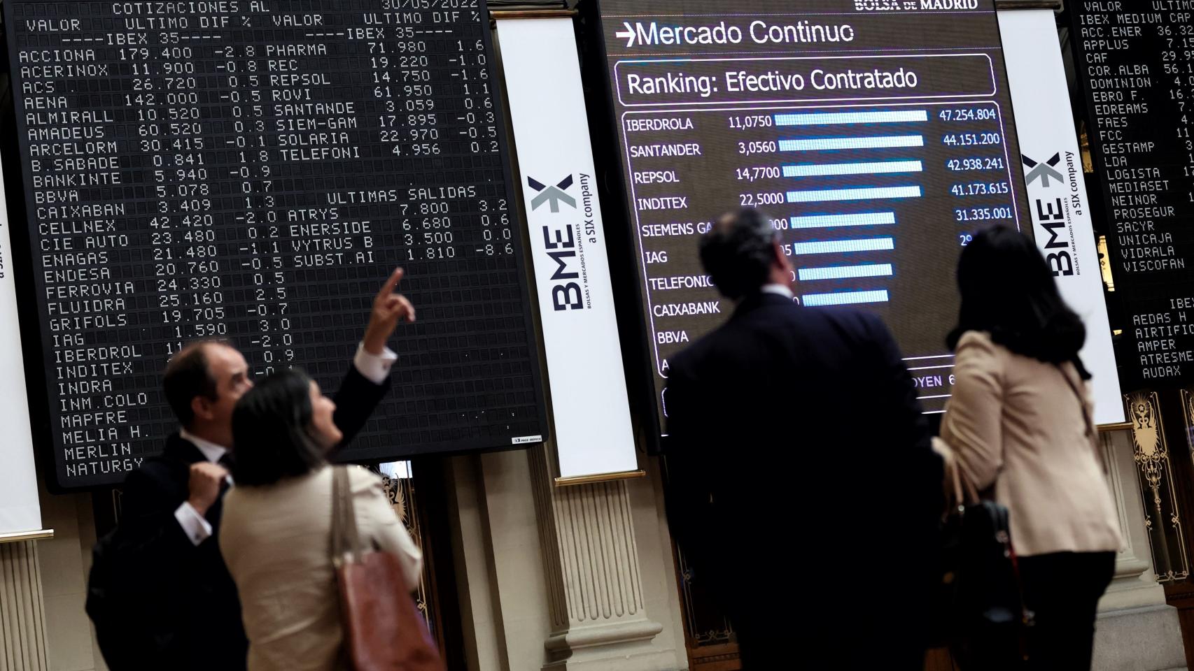 Cuatro personas frente a un antiguo panel de valores del Ibex 35 en el Palacio de la Bolsa.