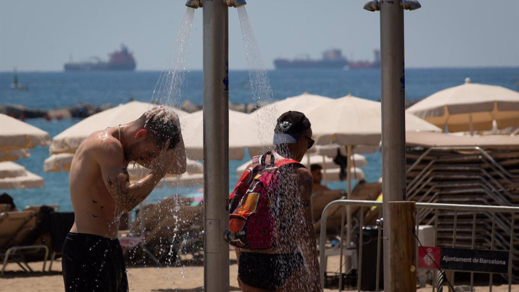 Varias personas se mojan en las duchas de playa.