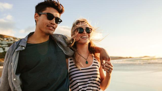 Una pareja caminando por la playa con sus gafas de sol.