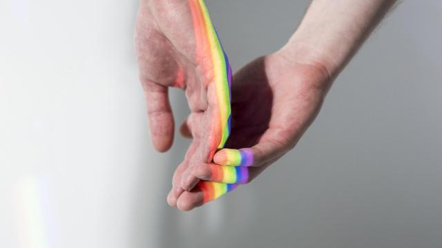 Las manos de dos hombres con el reflejo de la bandera LGTBI.