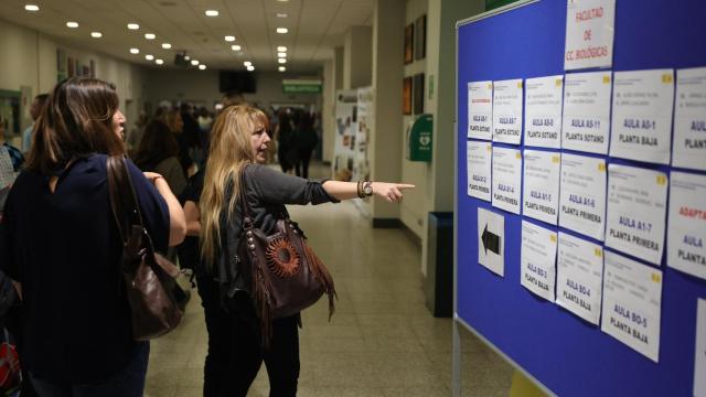Varias personas buscan en listados el aula donde van a realizar unas pruebas de acceso.