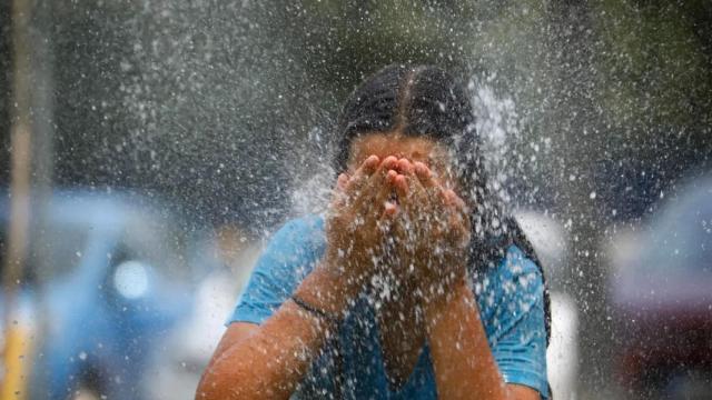 Una joven se refresca en una fuente durante una ola de calor.