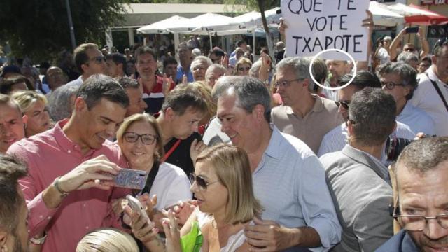 Pedro Sánchez junto a Juan Espadas en el sevillano barrio de Pino Montano, el 3 de septiembre de 2022. Al fondo, el creador anónimo del 'Que te vote Txapote' sujeta el cartel con el lema.