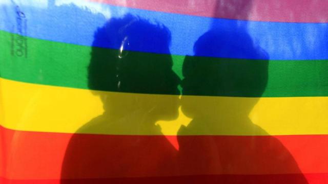Dos personas besándose frente a la bandera LGTBI, en imagen de archivo.