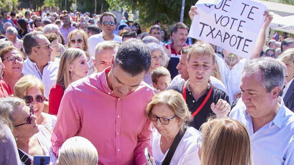 Pedro Sánchez junto a Juan Espadas en el sevillano barrio de Pino Montano, el 3 de septiembre de 2022. Al fondo, el creador anónimo del 'Que te vote Txapote' sujeta el cartel con el lema.