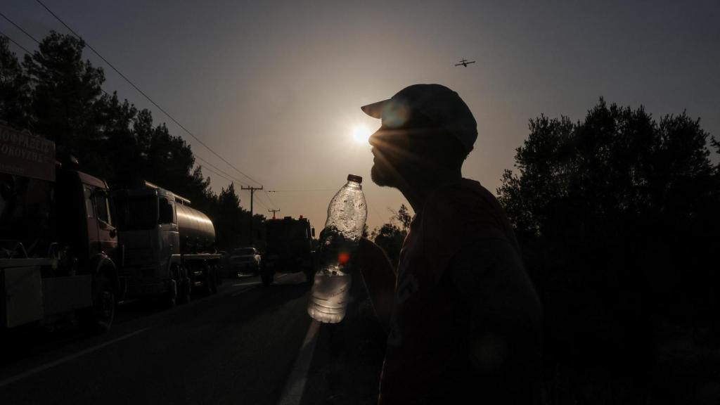 Un voluntario sostiene una botella de agua mientras arde un incendio forestal en el pueblo de Vati, en la isla de Rodas, Grecia..