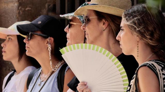 Varias personas se protegen del calor con gorras y abanico.
