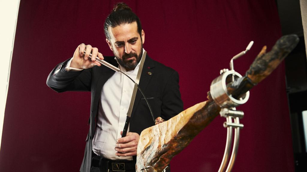 Emilio García cortando una pata de jamón con dos cuchillos.