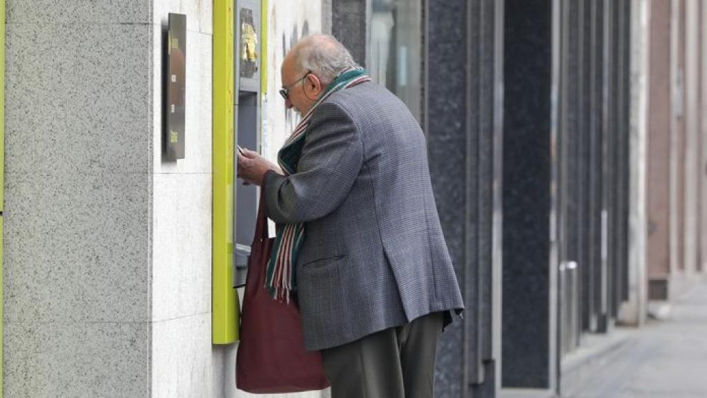 Un anciano sacando dinero de un cajero automático.