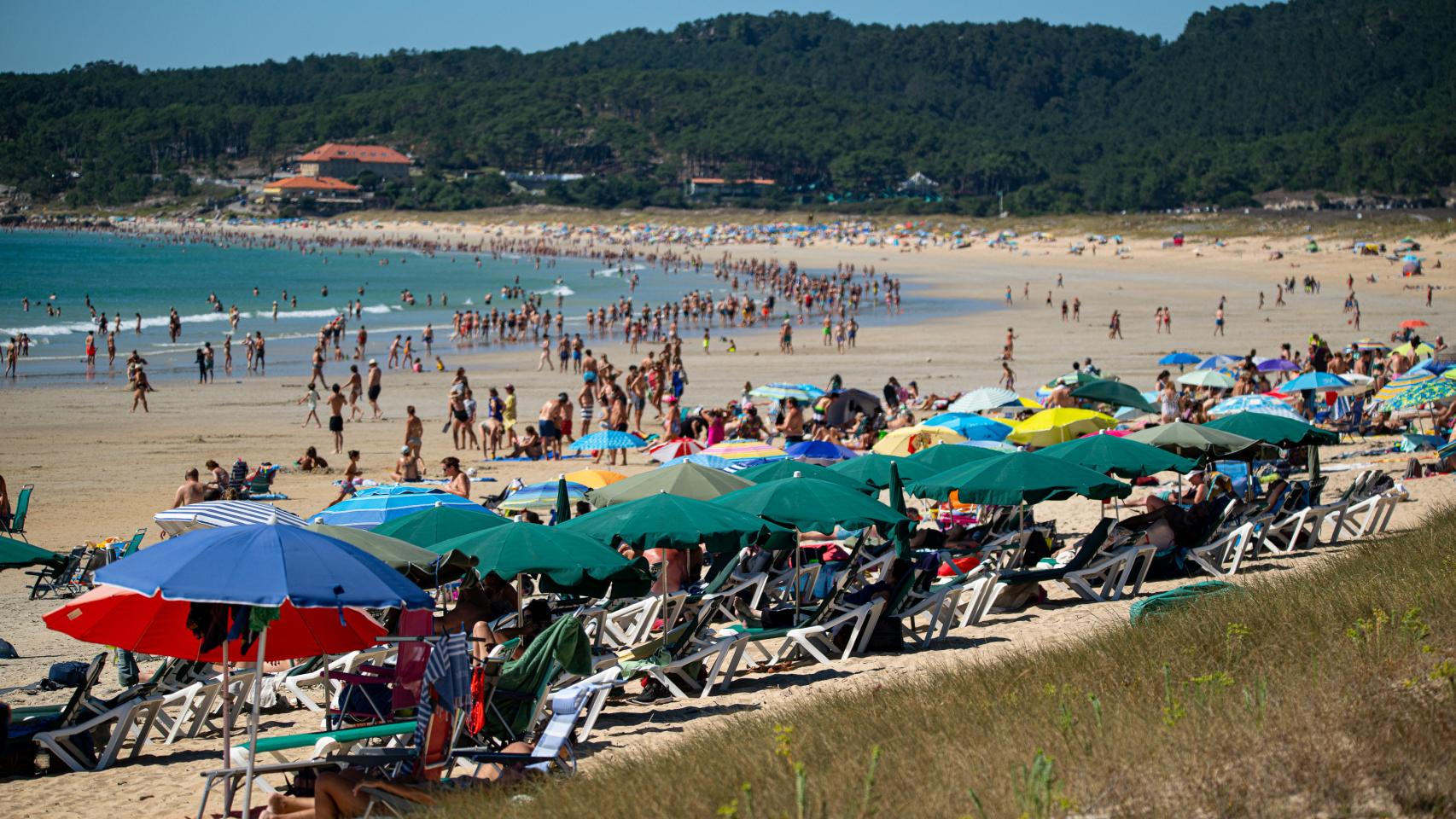 Varias personas se refugian del sol bajo sombrilla en una playa de Poneteveddra.