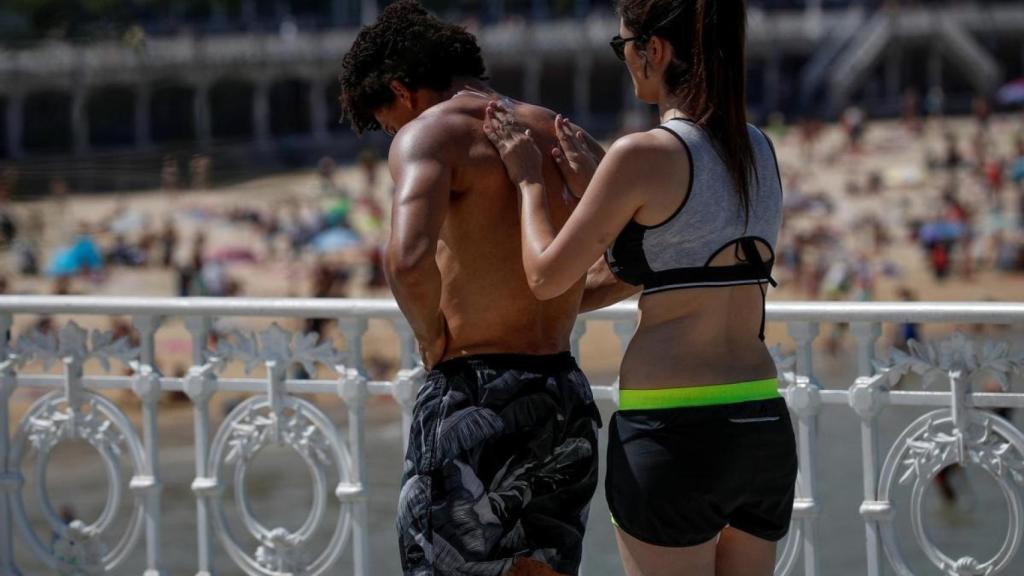 Una mujer le echa crema solar a un hombre.