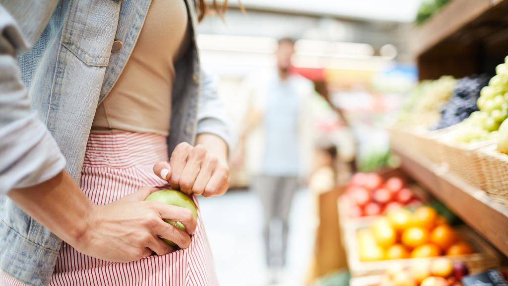 Una mujer roba una manzana en un establecimiento.