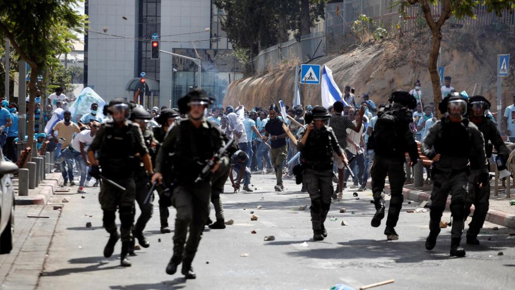 Los manifestantes sostienen palos y banderas cerca de miembros de las fuerzas de seguridad de Israel durante manifestaciones violentas en Tel Aviv, Israel.