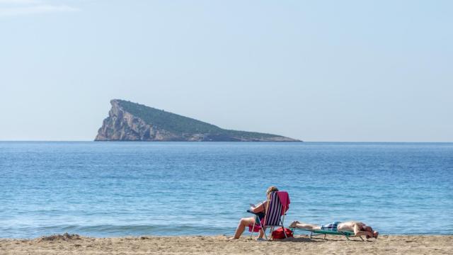 Dos personas disfrutan tomando el sol en una playa de Benidorm, Alicante