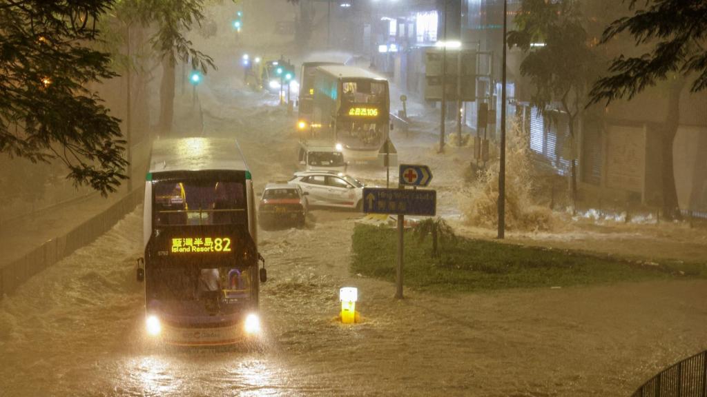 Un coche siendo arrastrado por el agua mientras un autobús avanza.
