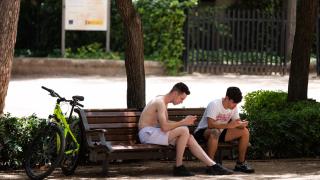 Two young people use their cell phones in a park.