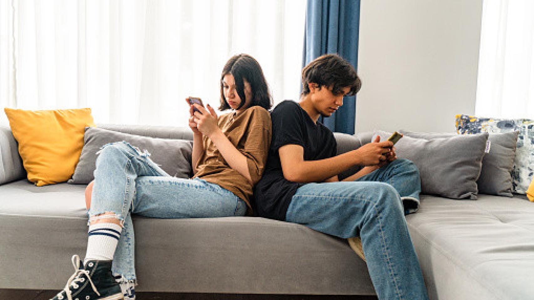 Imagen de una pareja joven dándose la espalda mirando el móvil.