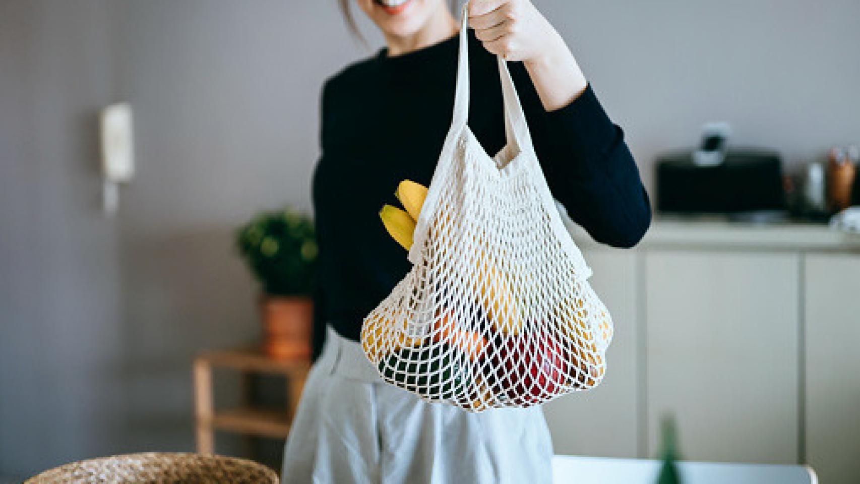 Imagen de una mujer sujetando una bolsa con verduras.