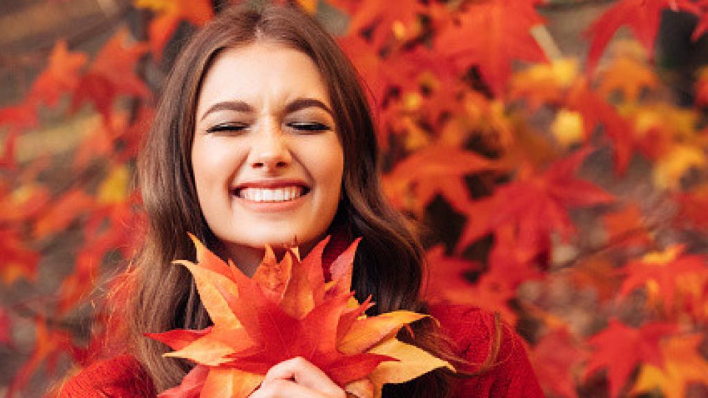 Imagen de una mujer sonriendo jugando con las hojas caídas de un árbol.