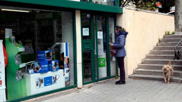 Una mujer con su perro frente a una farmacia