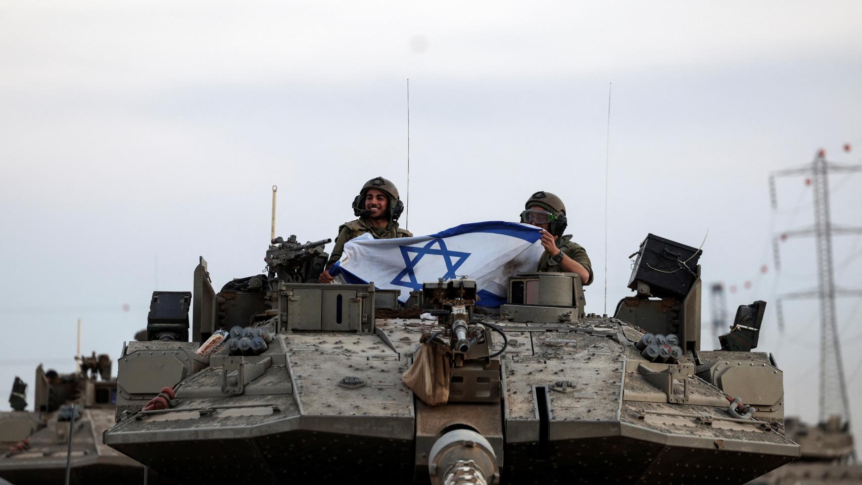 Soldados israelíes sostienen una bandera de Israel, cerca de la frontera con la Franja de Gaza.
