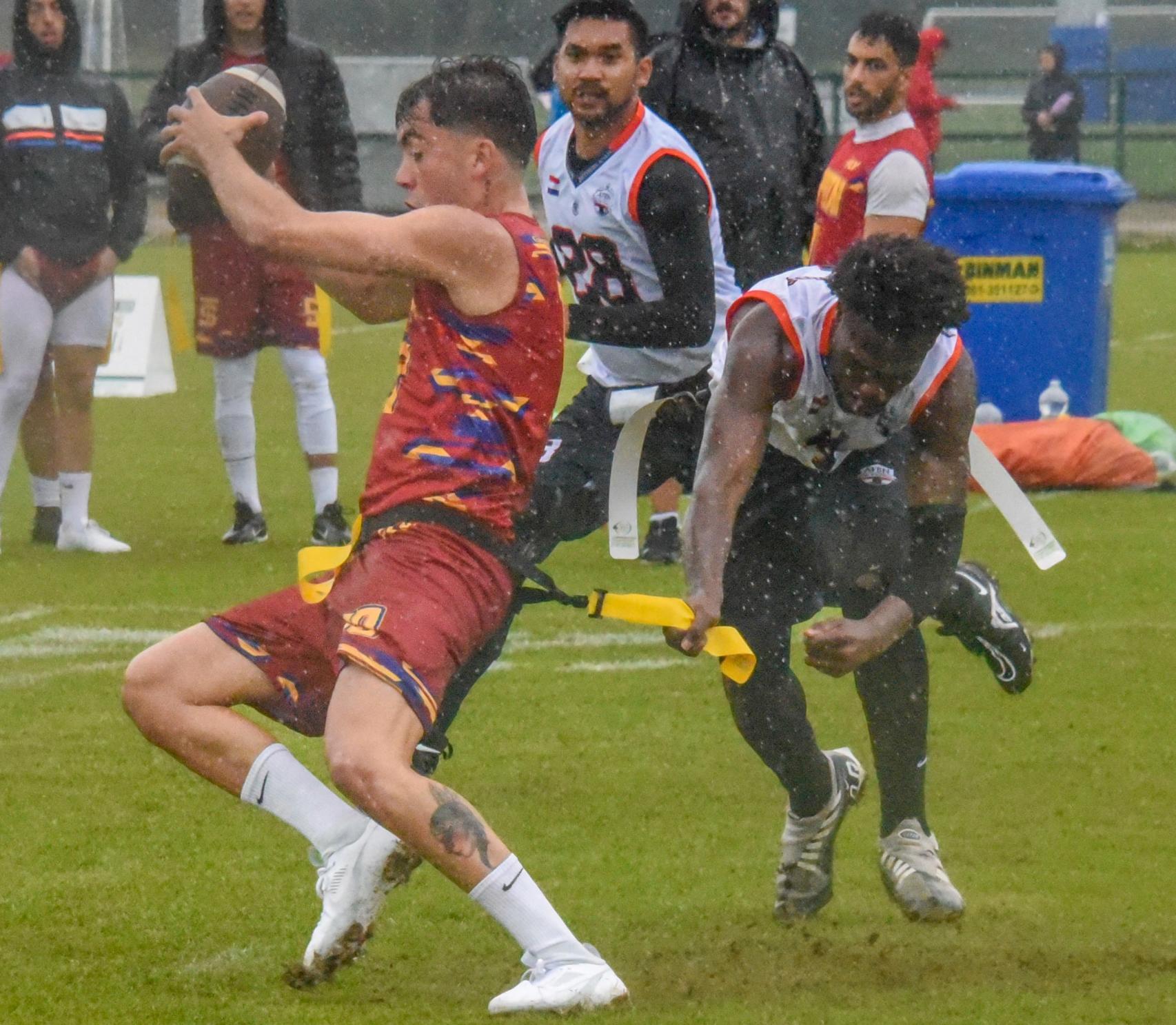 Un rival trata de detener a un jugador español bajo la lluvia.