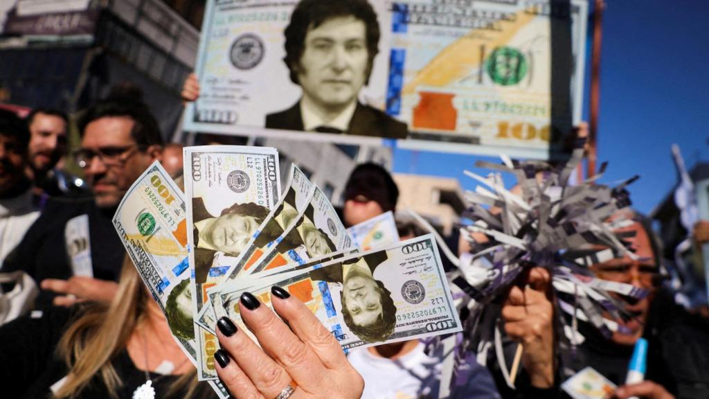 Simpatizantes de Milei sostienen billetes de dólar con su rostro durante un acto de campaña en Buenos Aires.
