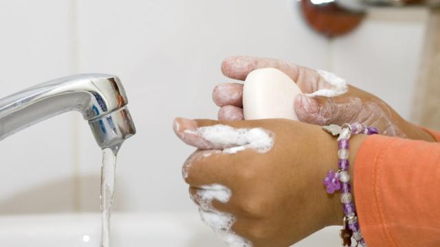 Una niña lavándose las manos delante de un grifo.