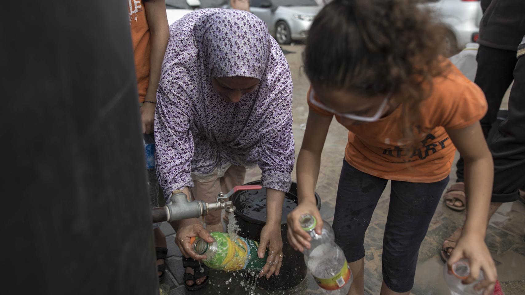 Niños gazatíes llenan botellas con agua en un campamento de refugiados del Programa de las Naciones Unidas para el Desarrollo (PNUD) en Khan Yunis.