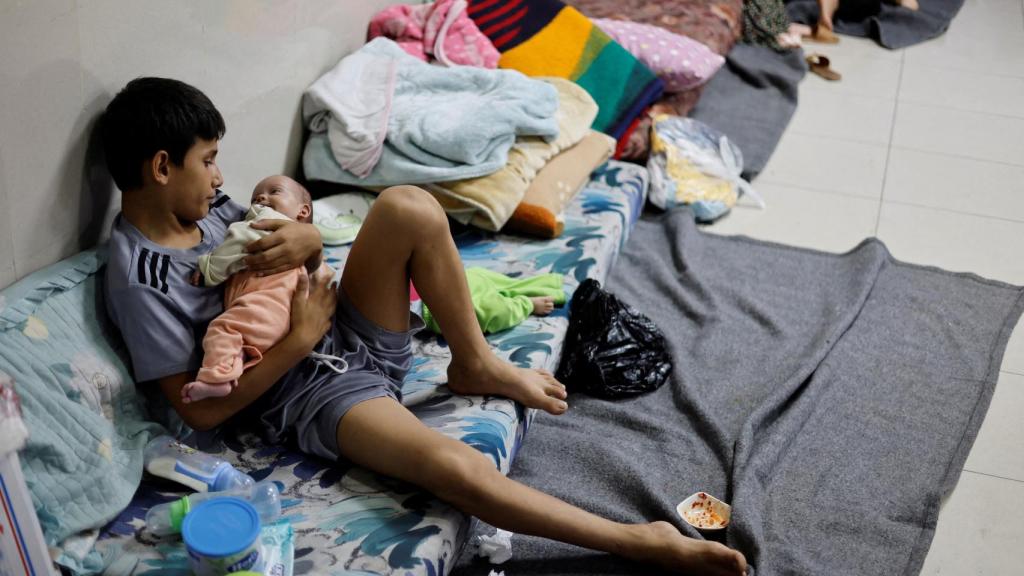 Un niño palestino desplazado cuida a sus hermanos gemelos mientras se refugian en el hospital Nasser en Khan Younis.
