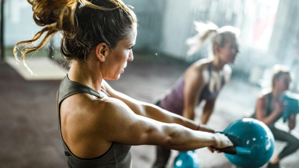 Una mujer en el gimnasio realizando ejercicios de fuerza para tonificar.