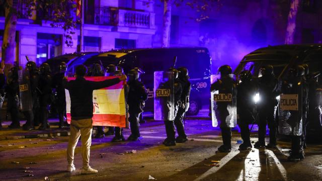 Un manifestante sostiene la bandera de España frente al cordón policial en la sede del PSOE en Ferraz.