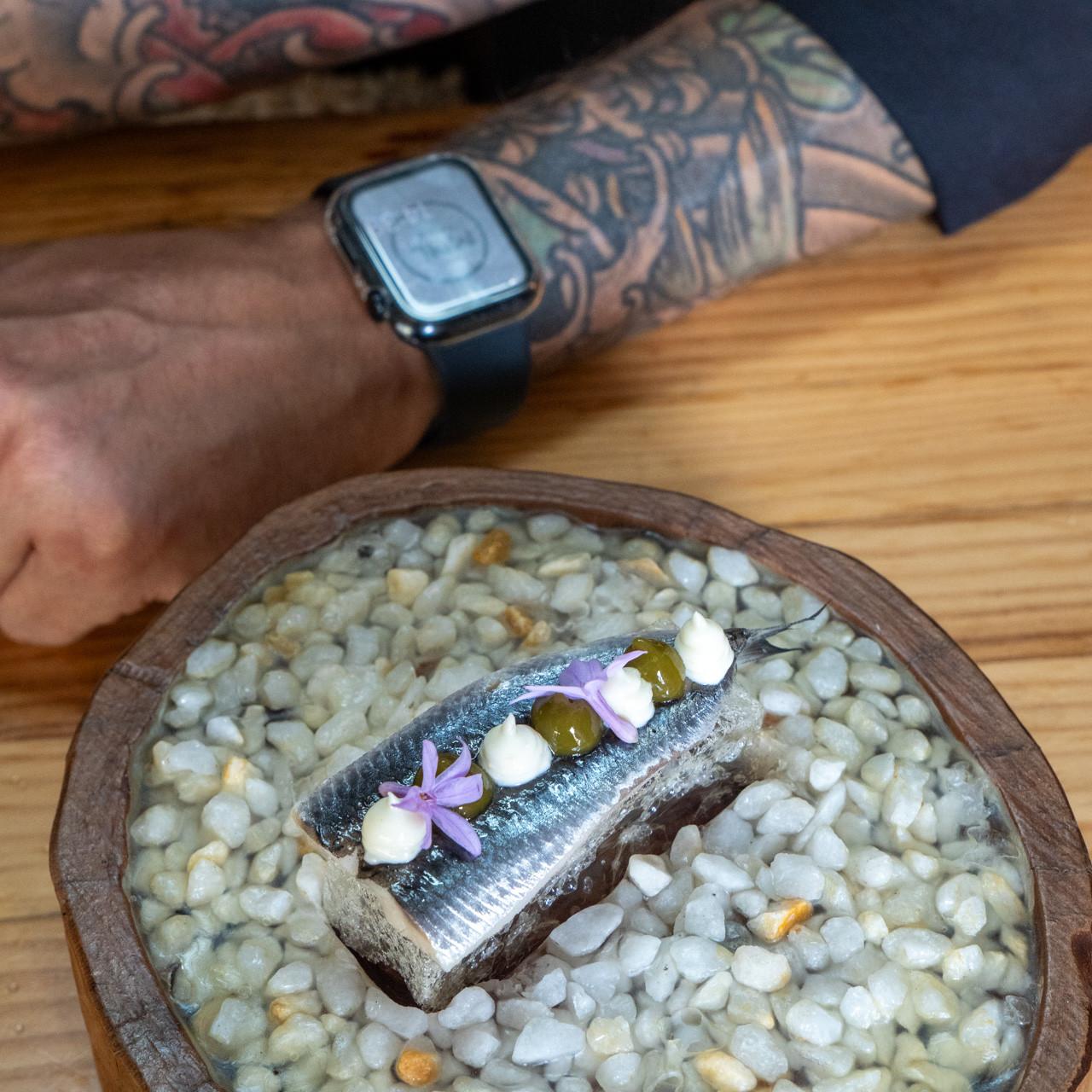 Los brazos del cocinero tatuados junto a una de sus creaciones.