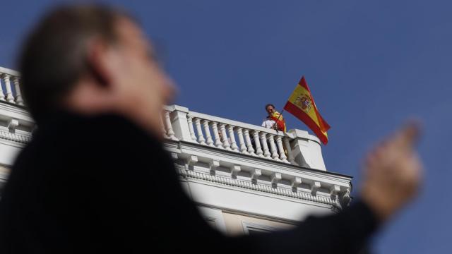 Un manifestante sigue el discurso del líder del PP Alberto Núñez Feijóo desde un balcón.
