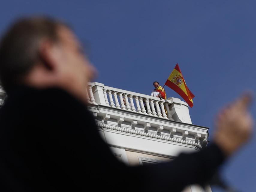 Un manifestante sigue el discurso del líder del PP Alberto Núñez Feijóo desde un balcón.