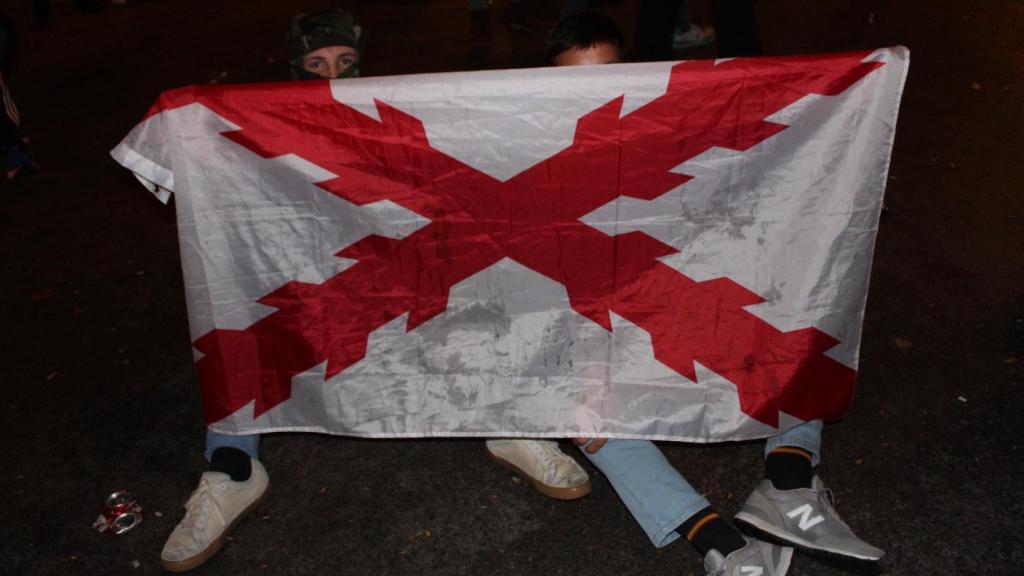 Dos jóvenes junto a una bandera con la Cruz de Borgoña