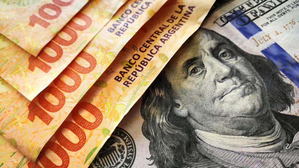 Varios billetes de 1000 pesos junto a uno de 100 dólares.