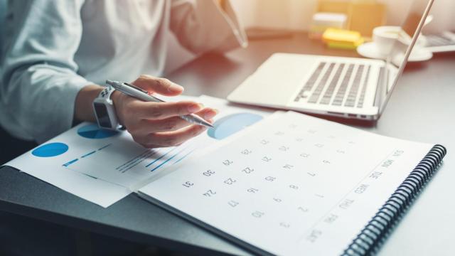 Mujer de negocios sentada trabajando y pensando para planificar el evento con calendario y portátil.