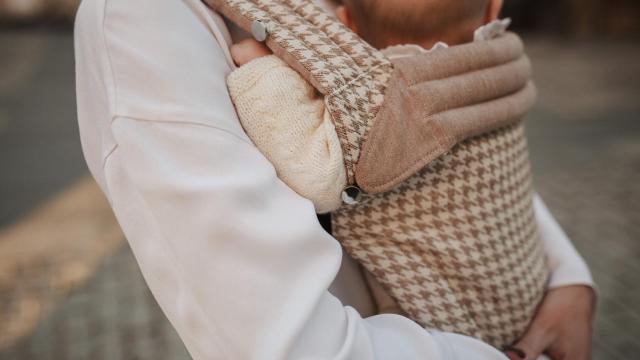 Madre cargando a su hijo según la práctica de porteo.
