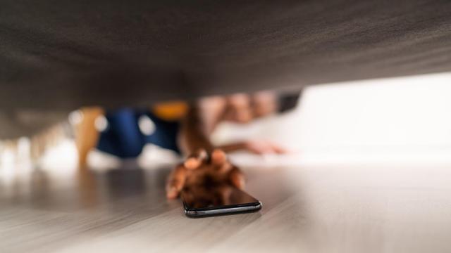Una persona buscando su teléfono móvil debajo del sofá.