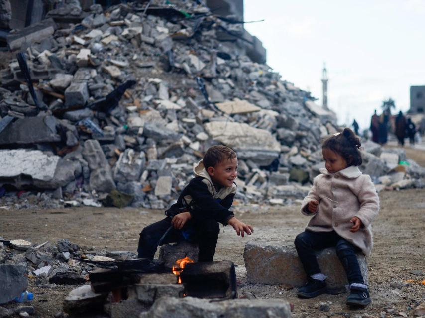 Dos niños juegan al calor del fuego junto a un edificio en escombros, este lunes en Jan Yunis.