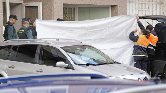 Dos agentes de Protección Civil tapan con una lona la zona donde se han encontrado los cuerpos en Oroso.