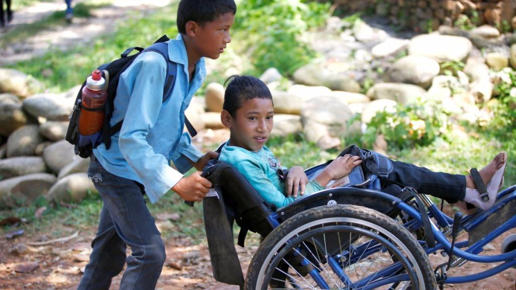 Un niño empuja la silla de ruedas de su compañero.