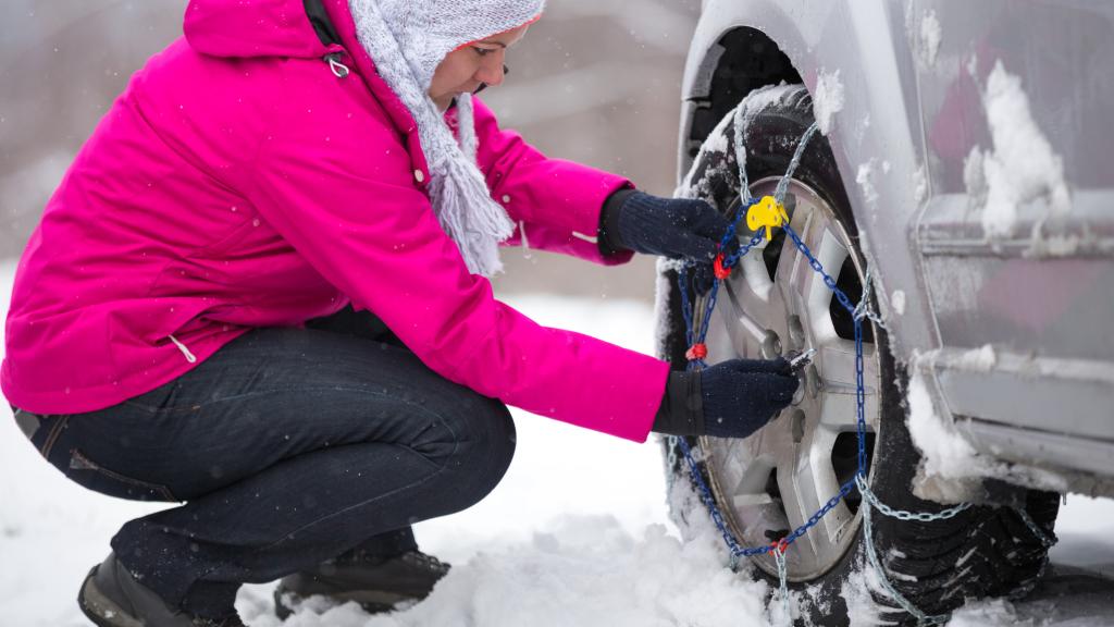Mujer colocando unas cadenas para la nieve en el coche