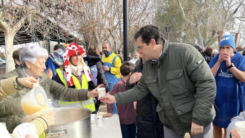 Una señora sirve un vaso de caldo caliente al presidente de la Diputación de Ciudad Real.