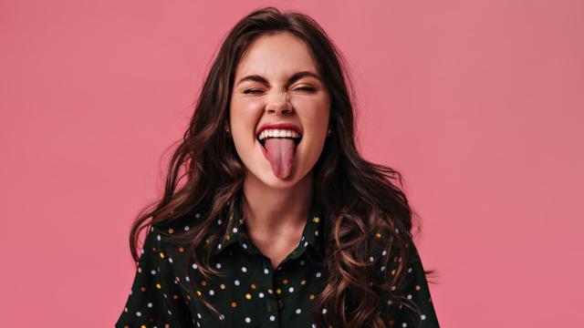 Mujer sacando la lengua con fondo rosa.
